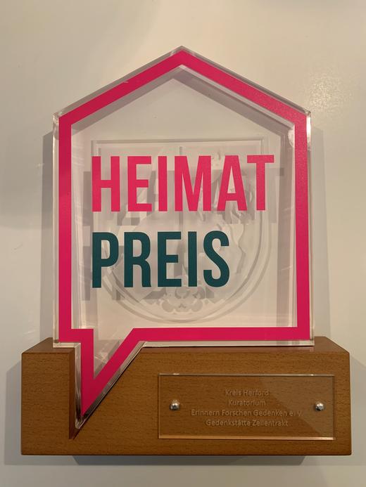 Heimatpreis Trophäe des Heimat-Preises Kreis Herford 2025 mit pinkem Rahmen und der Aufschrift „Heimatpreis“, verliehen an das Kuratorium Erinnern Forschen Gedenken e. V. für die Gedenkstätte Zellentrakt.
